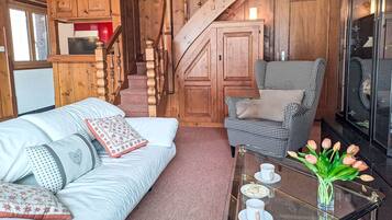 Ein gemütlicher Raum mit einer Holztreppe, einem Hundeprozess-Sessel, einem weißen Sofa und einem Glastisch mit einer Tulpenvase.