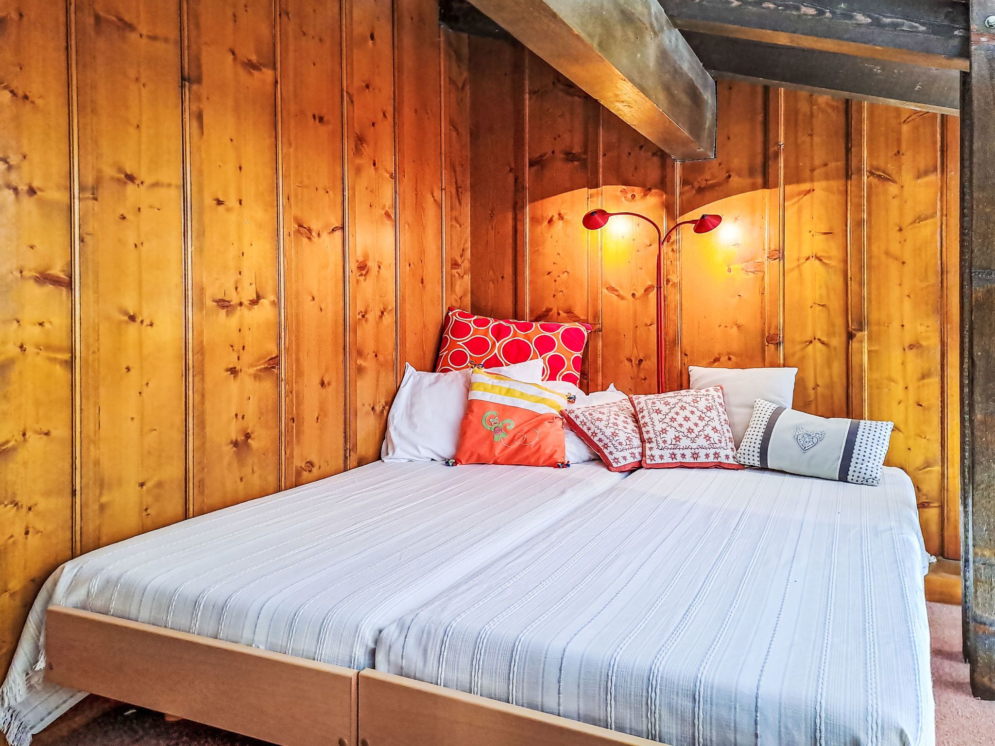 A wooden-paneled room with a bed, pillows, and a wall-mounted light fixture.