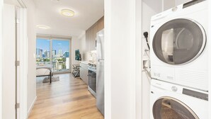 A modern kitchen with a built-in washer and dryer, a dining area with a view of the city, and a spacious living room with a large window. - Chic Studio with Skyline Views at The Park on Keeaumoku (Honolulu)