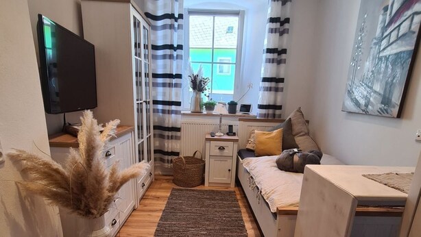 A compact living space with a bed, a desk, a TV, and a window with curtains. - Kraxler Single by Interhome (Weißenstadt)