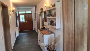 A hallway with a wooden door at the end, a white cabinet with a vase of dried flowers, and a shelf with various items. - Kraxler Single by Interhome (Weißenstadt)