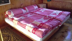 Ein Doppelbett mit kariertem Überwurf und Kissen, Holzboden, ein kleiner Nachttisch und ein Fenster mit Vorhängen.