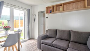 Ein modernes Wohnzimmer mit grauem Sofa, Holzregalen, einer Essecke mit Tisch und Stühlen und Blick ins Freie.