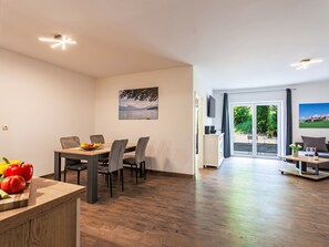 A modern living room with a dining area, wooden flooring, and a view through glass doors to an outdoor area. - Alpenlodge Hochvogel by Interhome (Lechbruck am See)