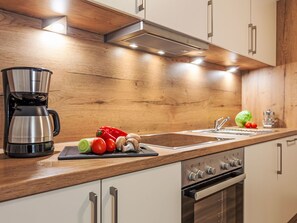 Una cocina moderna con armarios de madera, una cafetera de acero inoxidable, un fregadero y una estufa.