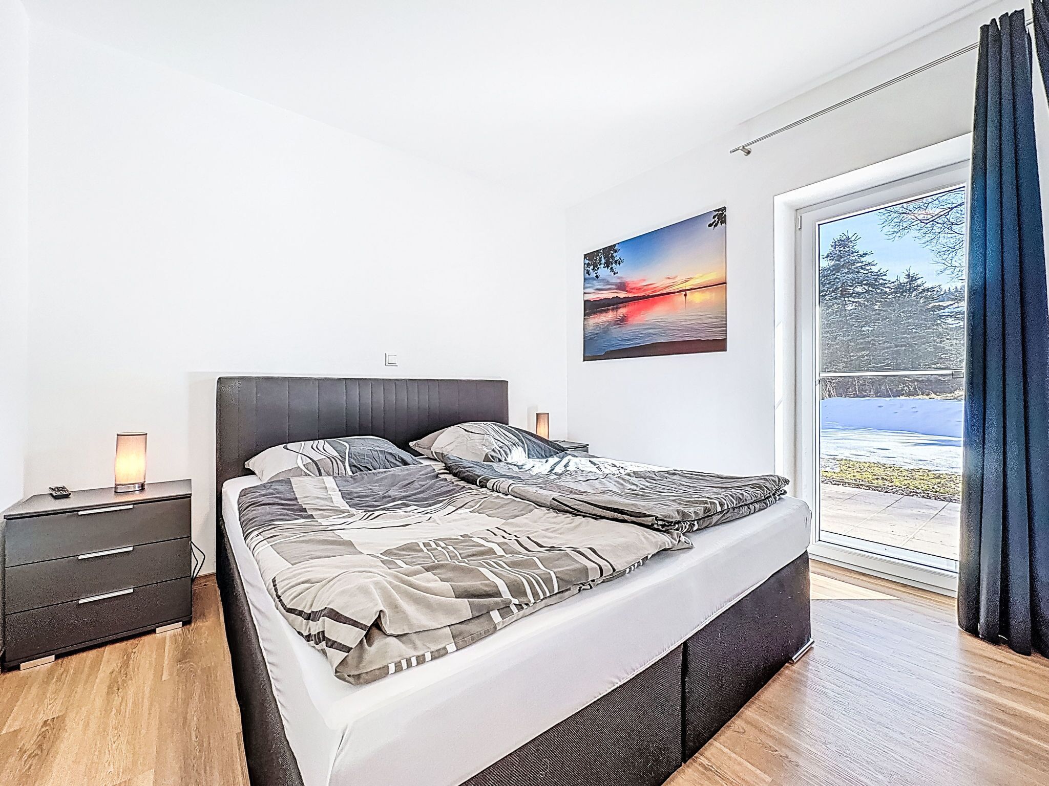 Una camera da letto moderna con un letto, comodini, un tavolino e una finestra con tende, oltre a un quadro appeso al muro.