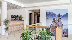 Eine Lobby mit Holzbude, Zimmerpflanzen, einem großen Landschaftsbild und einer Treppe.