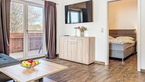 Ein modernes Zimmer mit Holzboden, einem Esstisch mit Früchten, einem Schrank, einem Bett und einem Fernseher an der Wand.