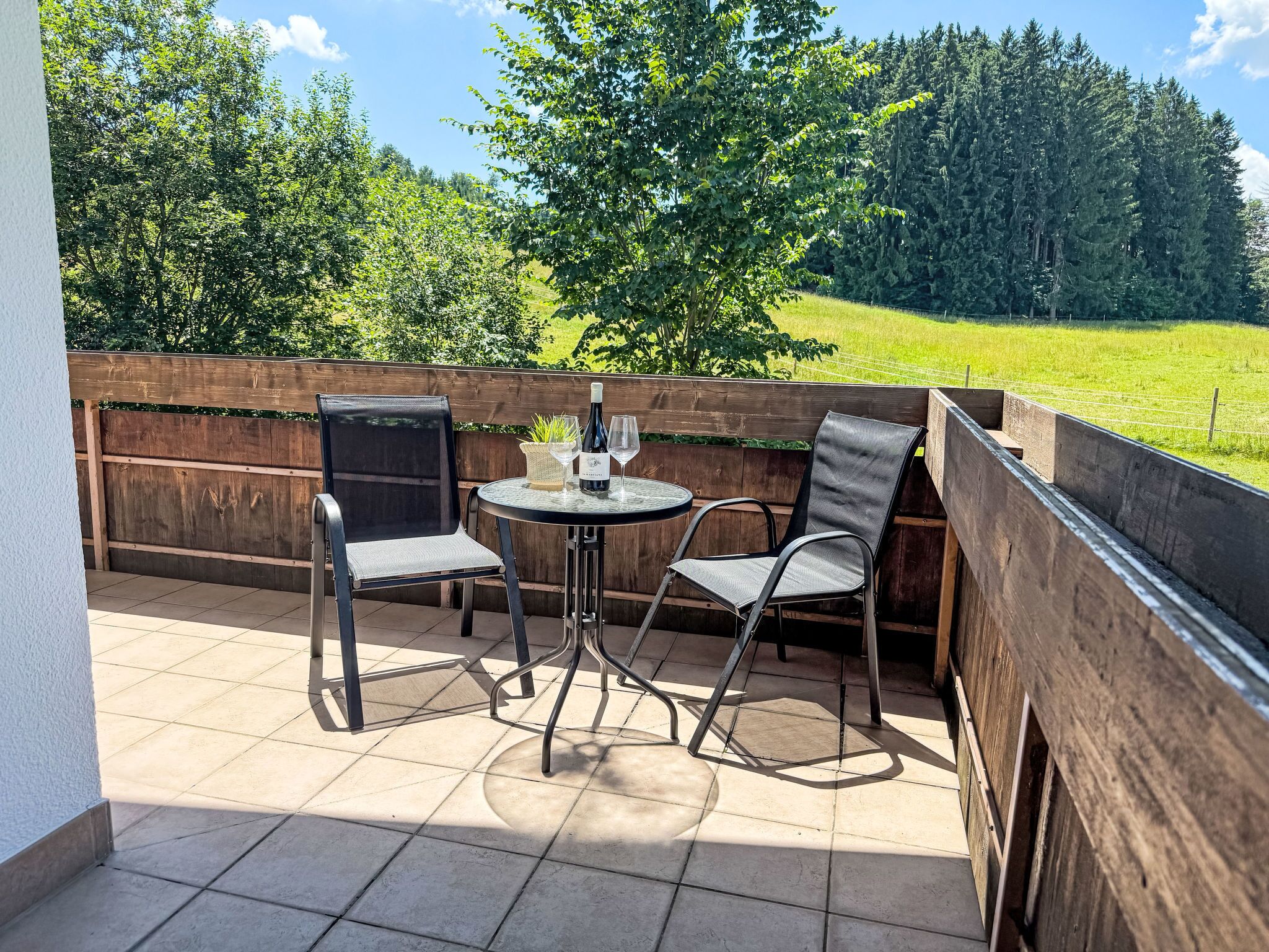Une terrasse avec deux chaises et une table, une bouteille de vin et une petite plante.