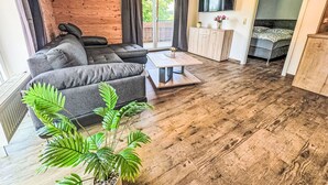 Ein modernes Wohnzimmer mit einem Ecksofa, einem Couchtisch, einem an der Wand befestigten Fernseher und einem Bett im angrenzenden Raum.