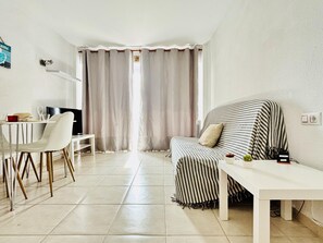 Ein modernes Wohnzimmer mit einem gestreiften Sofa, einem weißen Tisch, einem Fernseher und einem Essbereich mit Stühlen.