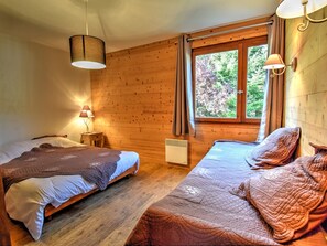 A cozy room with two beds, wooden walls, a window with curtains, and a hanging lamp. - Lovely apartment in Morzine with parking near the center (Morzine)