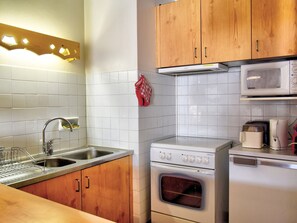 A kitchen with wooden cabinets, a stainless steel sink, a microwave, a toaster, and an oven. - Lovely apartment in Morzine with parking near the center (Morzine)