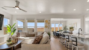 Ein geräumiges Wohnzimmer mit großem Sofa, einer Essecke mit Barhocker und einer Küche mit weißer Arbeitsplatte.