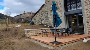 Un bâtiment en pierre doté d’un patio comprenant une table, des chaises et un parasol bleu.