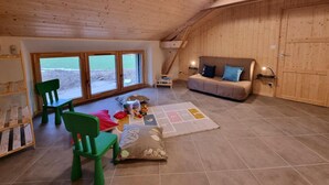 Un intérieur en bois comprenant un canapé, des fauteuils, un espace de jeux et une vue dégagée grâce à de grandes fenêtres.
