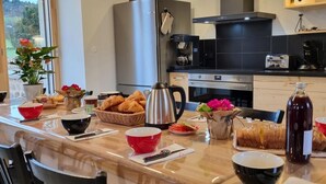 Une cuisine moderne équipée d’un réfrigérateur en acier inoxydable, d’une machine à café et d’une étagère en bois au-dessus du plan de travail.