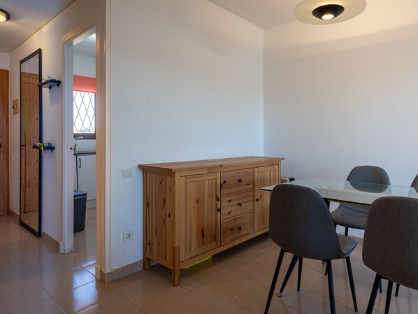 A room with a wooden cabinet, a dining table with chairs, and a view of a window and a door. - 2BR Apartment in Creixell with Pool & Parking, 5min to Beach (Creixell)