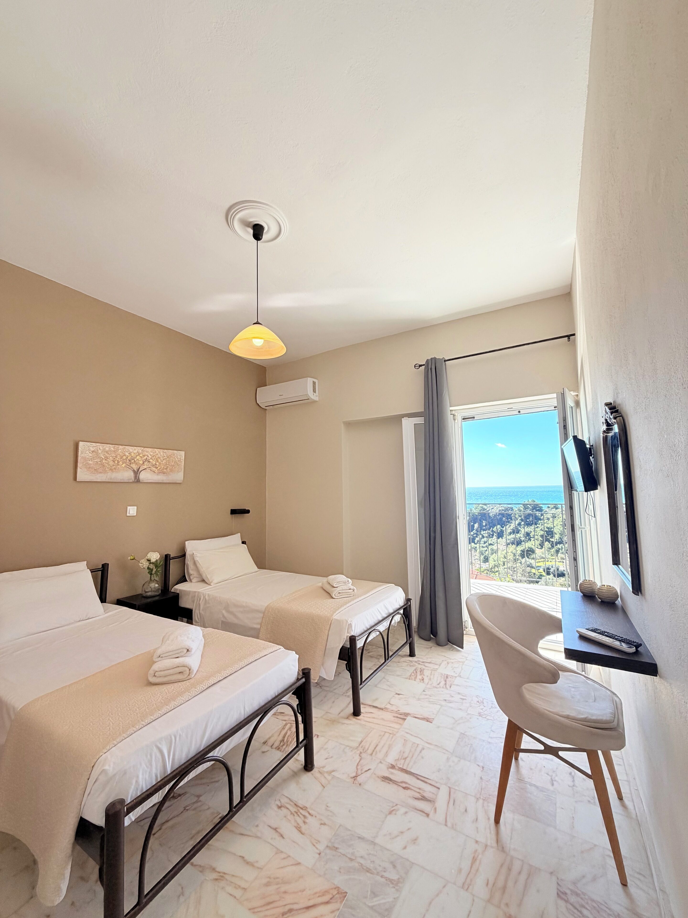 A hotel room with two beds, a desk, a chair, a TV, and a view of the landscape.