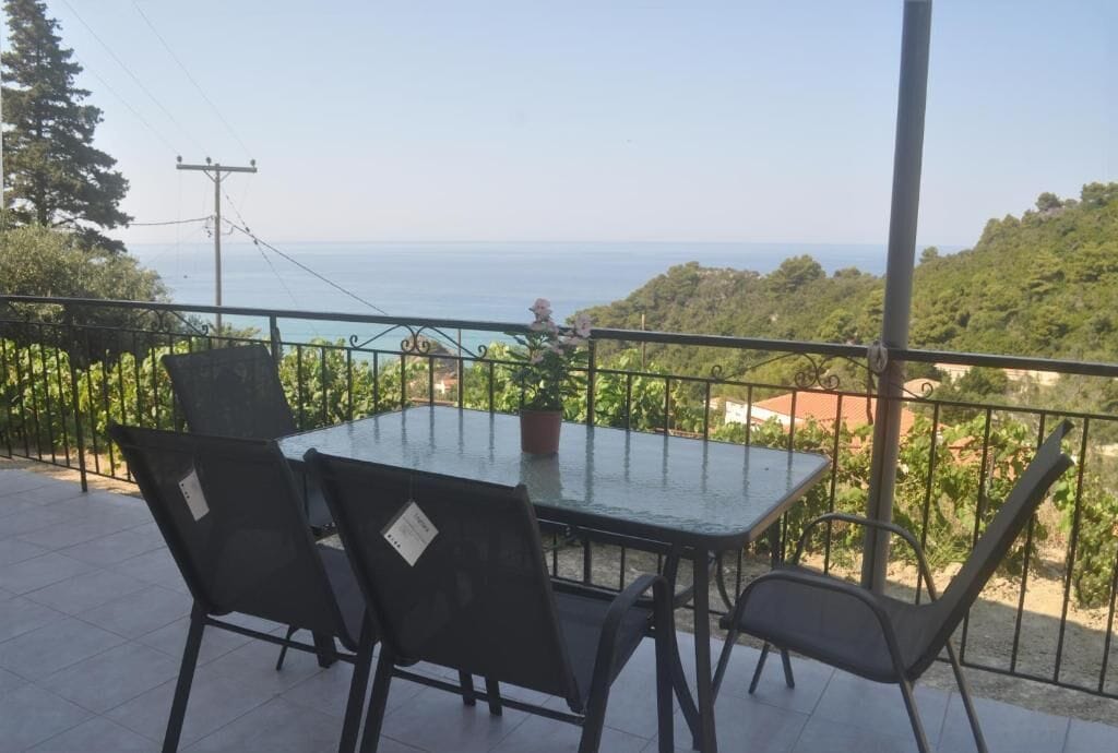 A terrace with a table and chairs, overlooking a coastal landscape.