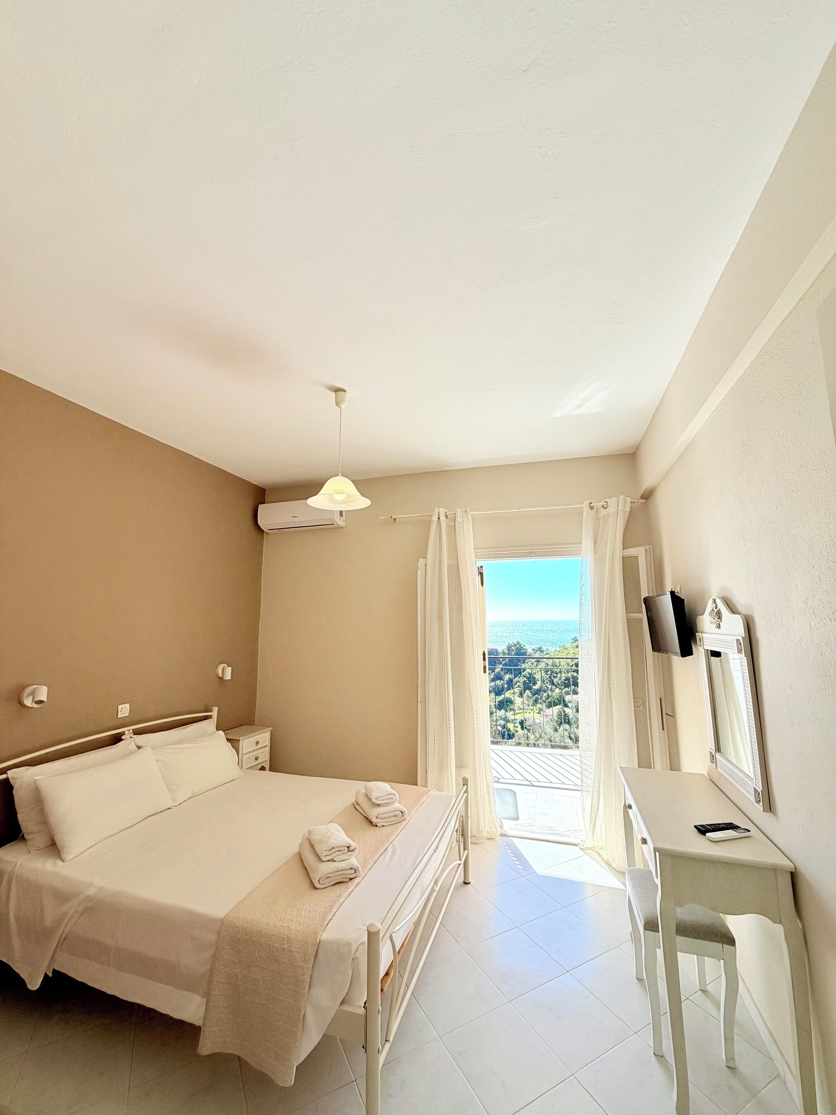 Ein Schlafzimmer mit einem Bett, Nachttischen, einem Schreibtisch, einem Spiegel und Blick ins Freie.