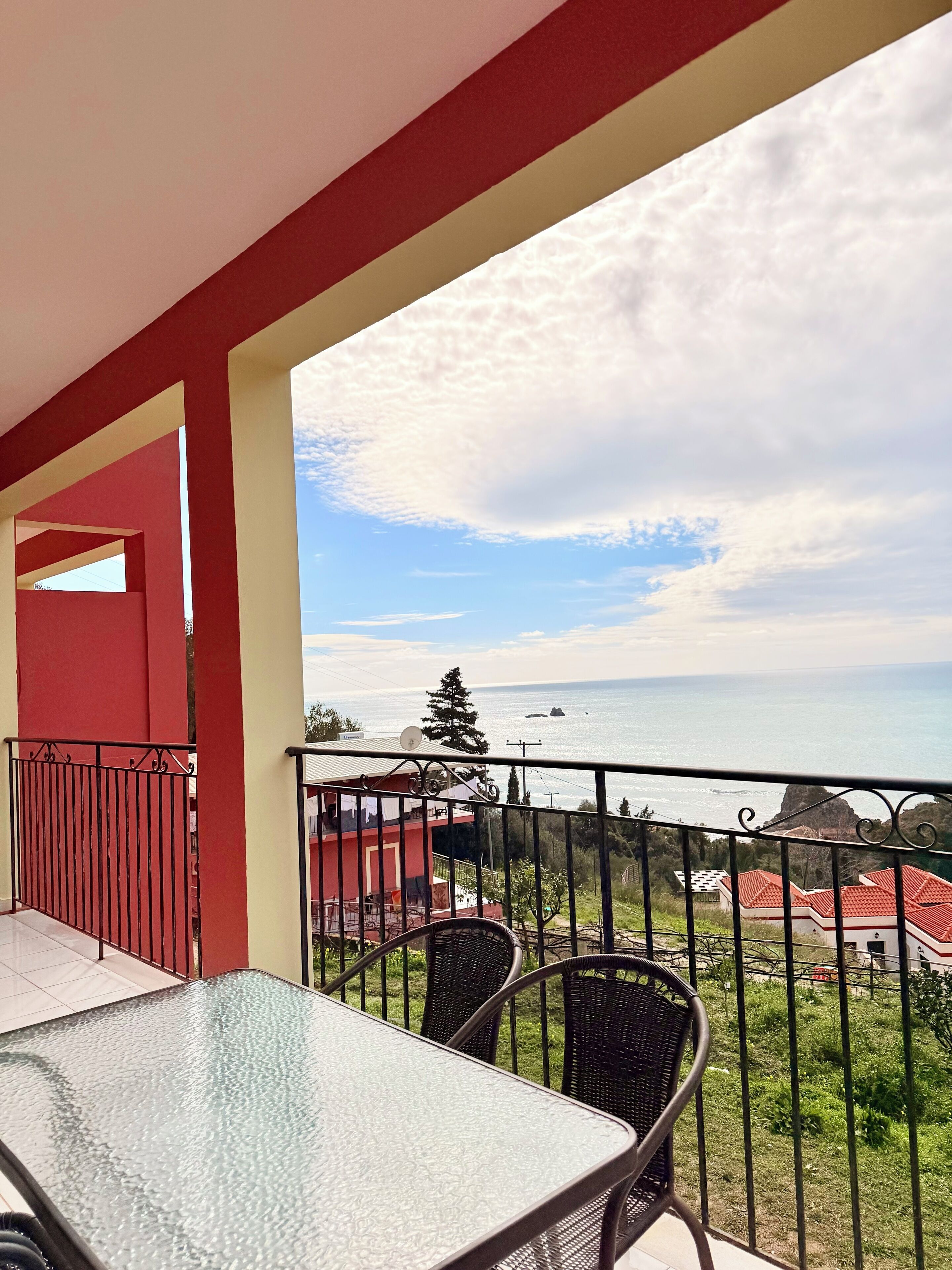 Balcón con mesa y sillas, con vistas a la costa, casas y vegetación.
