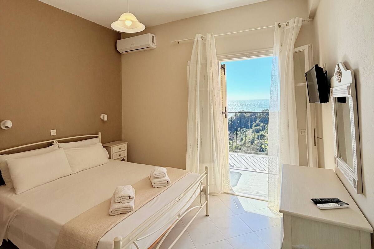 A bedroom with a bed, bedside tables, a desk, and a view of the outdoors.