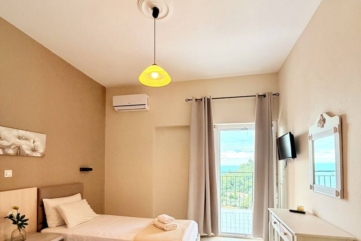 A hotel room with two beds, a desk, a TV, and a balcony with a view.