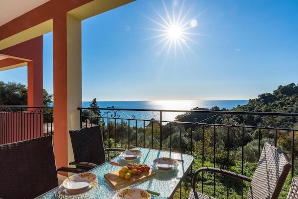 Un balcón con una mesa dispuesta para una comida, con vistas a un paisaje costero.