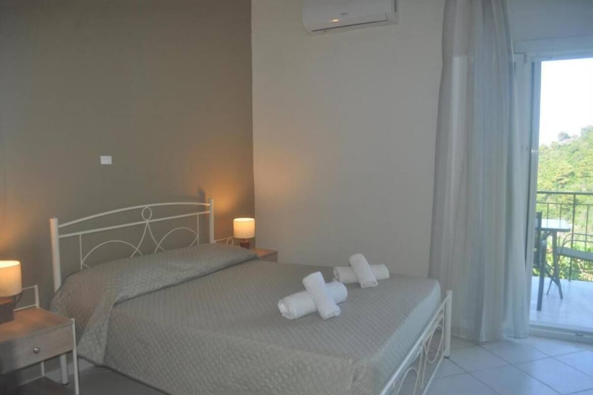 A neatly made bed with a white headboard, two bedside lamps, and a balcony with a table and chairs.