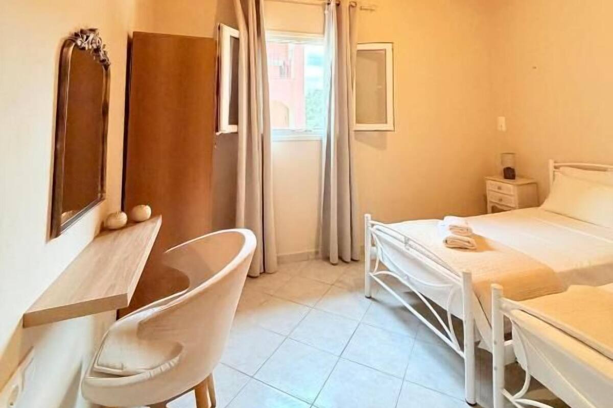 A small, cozy room with a wooden ceiling, a single bed, a desk with a chair, and a window with curtains.