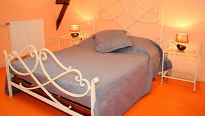 Ein Schlafzimmer mit weißem Metallbettgestell, grauer Bettdecke, zwei Nachttischlampen und einem Heizkörper.