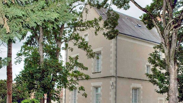 Ein zweistöckiges Gebäude mit einer symmetrischen Fassade, großen Fenstern und einem zentralen Eingang mit Stufen.