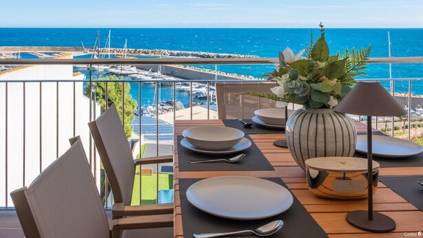 Un balcón con una mesa dispuesta para comer, con vistas a un puerto deportivo y al mar.