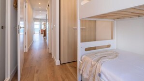 Una habitación con literas, piso de madera y un pasillo que conduce a otra habitación.