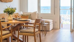Un comedor con una mesa dispuesta para dos, un sofá y vista al mar a través de amplios ventanales.