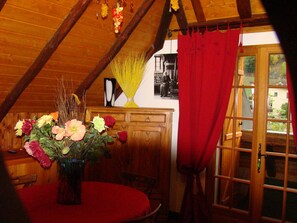 Ein gemütliches Zimmer mit Holzbalkendecke, einem roten Vorhang und einem Tisch mit Blumen in einer Vase.