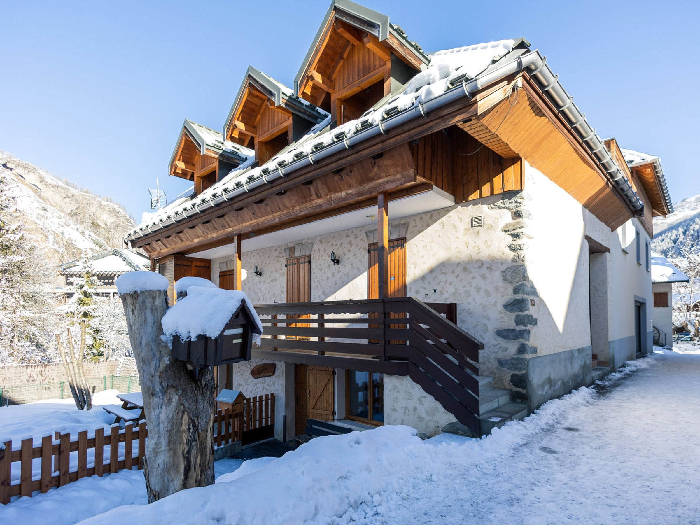 A chalet-style building with a stone facade, wooden balconies, and a wooden staircase leading to the entrance.