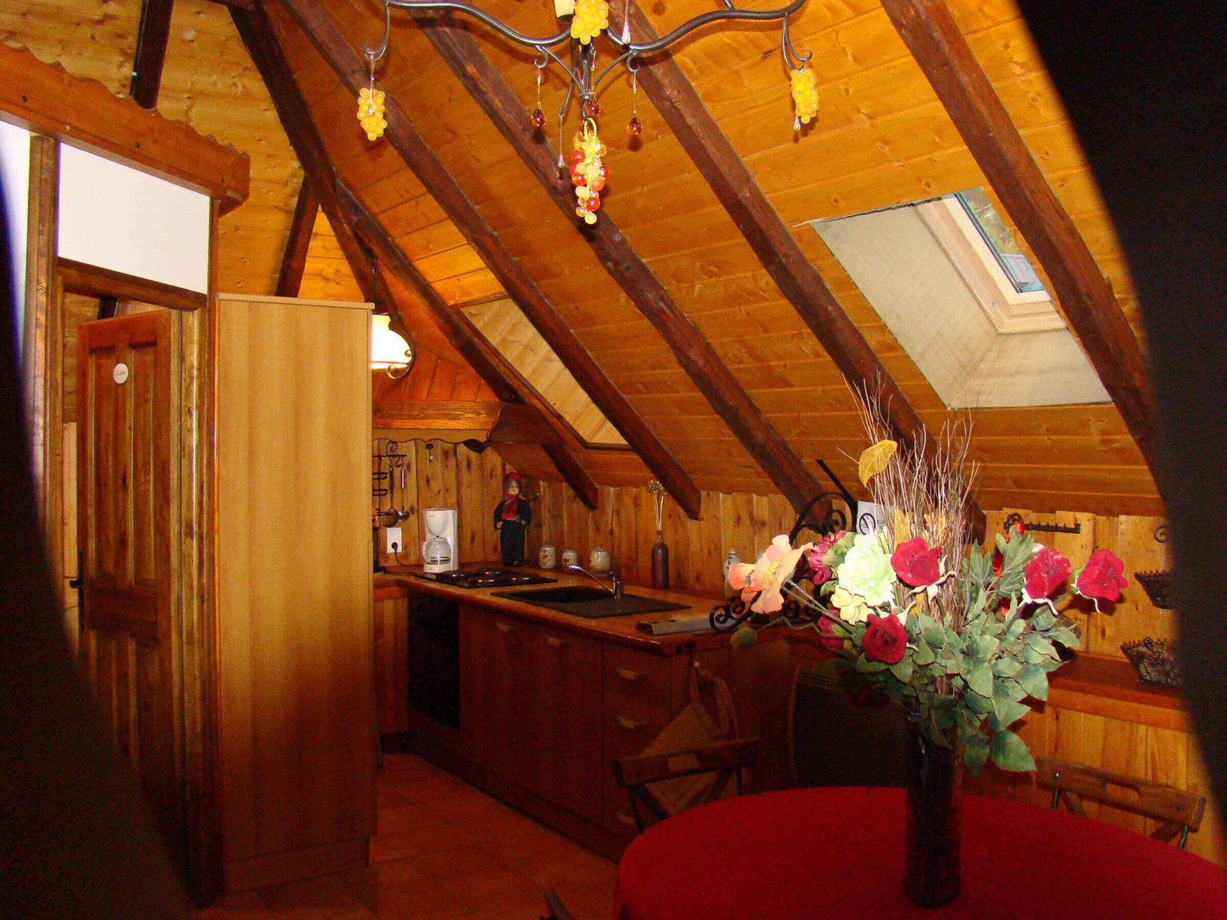 A cozy attic room with wooden beams, a red table, and a vase of flowers.