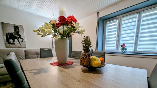 A dining area with a wooden table, a vase with flowers, and a fruit bowl. - Spacious Gîte in Selles, 3 Bedrooms, Garden, Family-Friendly (Selles)