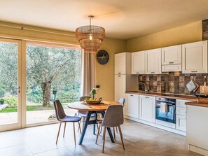 Eine moderne Küche mit weißen Schränken, einem Holztisch und einem großen Fenster mit Blick auf einen Garten.