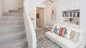 Ein modernes Interieur mit einer weißen Treppe, einem weißen Sofa mit gemusterten Kissen, einer Küchenzeile und einem Bücherregal.