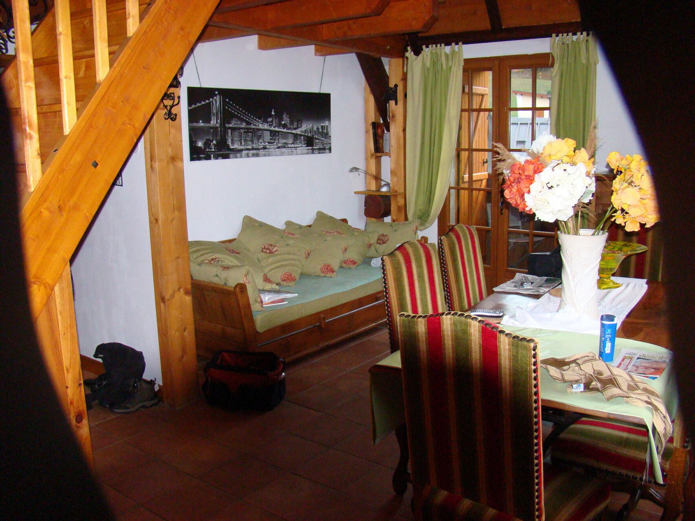 A cozy room with a wooden staircase, a bed with floral bedding, striped chairs, a table with a vase of flowers, and a framed picture on the wall.