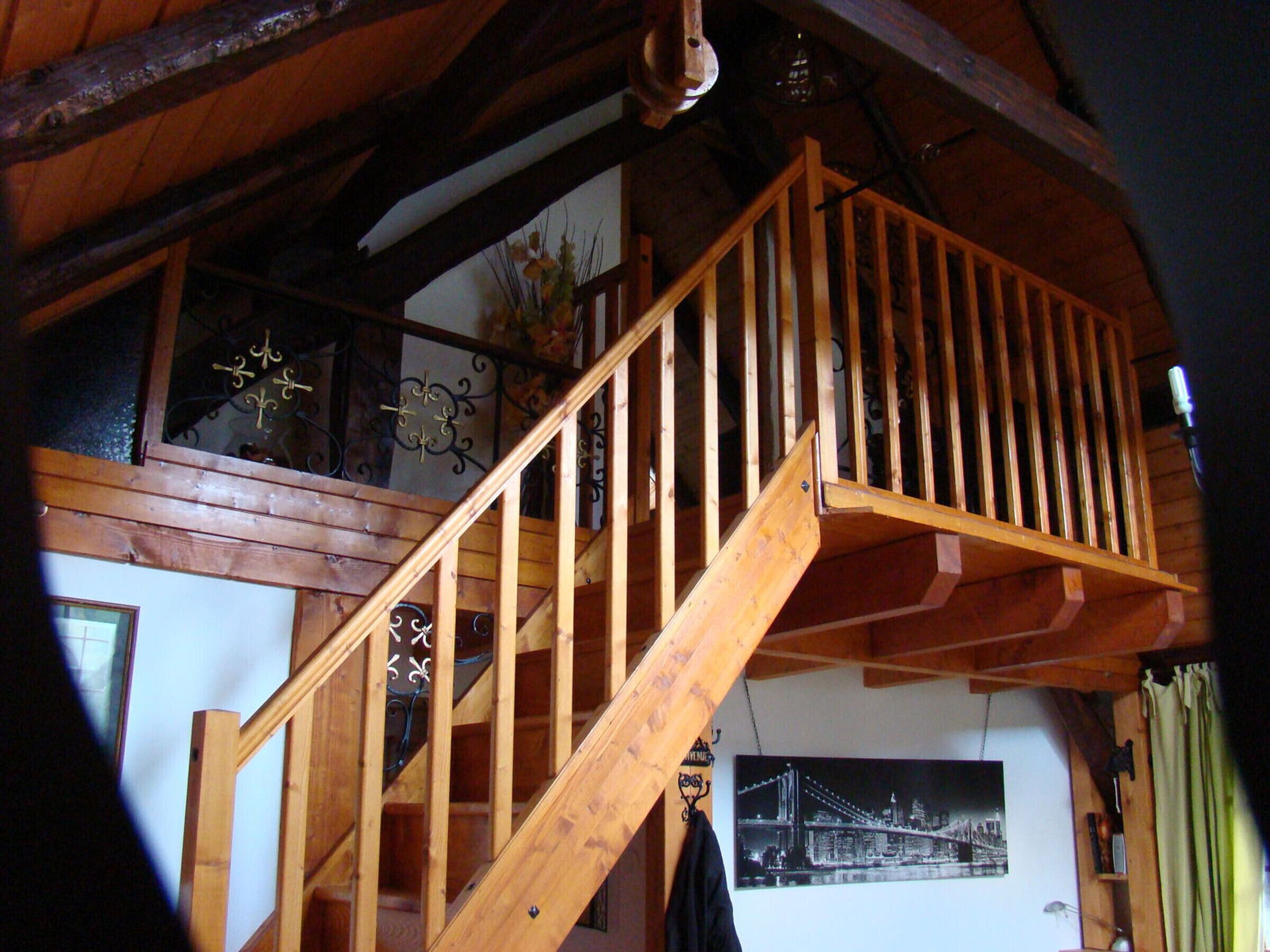 A wooden staircase with a railing, a chandelier, and a framed picture on the wall.