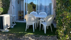 Un patio con mesa y sillas, una puerta corrediza de vidrio y un pequeño jardín.