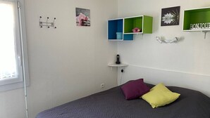 Un dormitorio con cama, dos almohadas, una mesita de noche, un teléfono en la pared y una ventana.