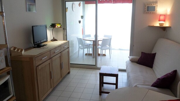Una sala de estar moderna con un televisor de pantalla plana, armarios de madera, un sofá y un comedor con sillas y una mesa.