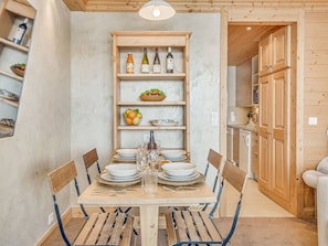 Ein Essbereich mit einem Holztisch, gedeckt für vier Personen, umgeben von Stühlen. Darüber befindet sich ein Holzregal mit Weinflaschen und Obstschalen.