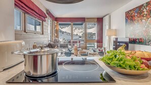 Eine moderne Küche mit einem großen Herd, einer Schüssel frischem Grünzeug und Blick auf verschneite Berge durch die Fenster.