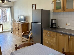 Une cuisine compacte équipée d’un réfrigérateur, d’une machine à café, de meubles de rangement en bois et d’un coin repas avec une table et des chaises.